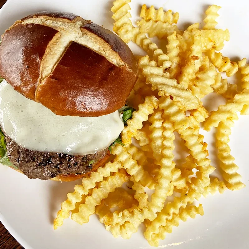 Cheeseburger with pretzel bun, melted cheese, and crinkle-cut fries.
