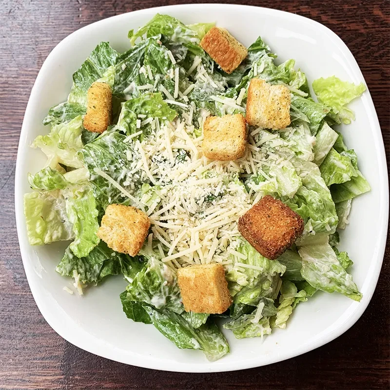 Overhead close-up of a Caesar salad with romaine, croutons, and Parmesan.
