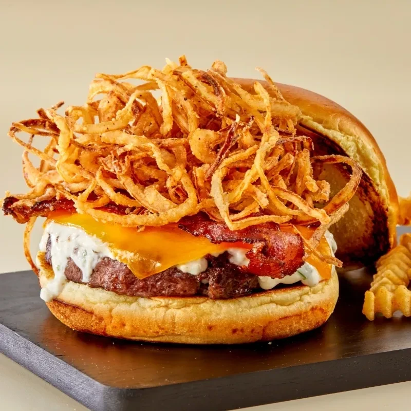 Gourmet burger with bacon, melted cheese, creamy sauce, fried onions, and fries.
