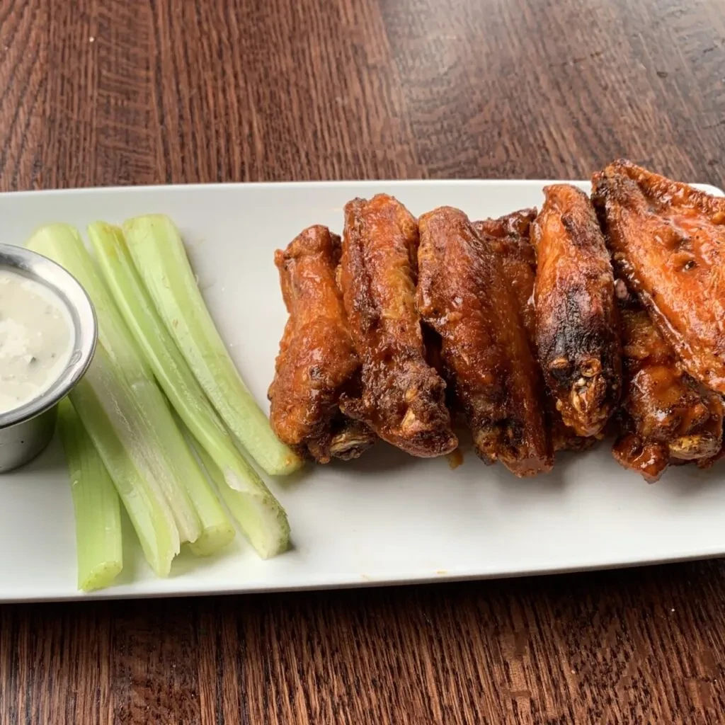 Crispy chicken wings, celery sticks, and dipping sauce on a plate.