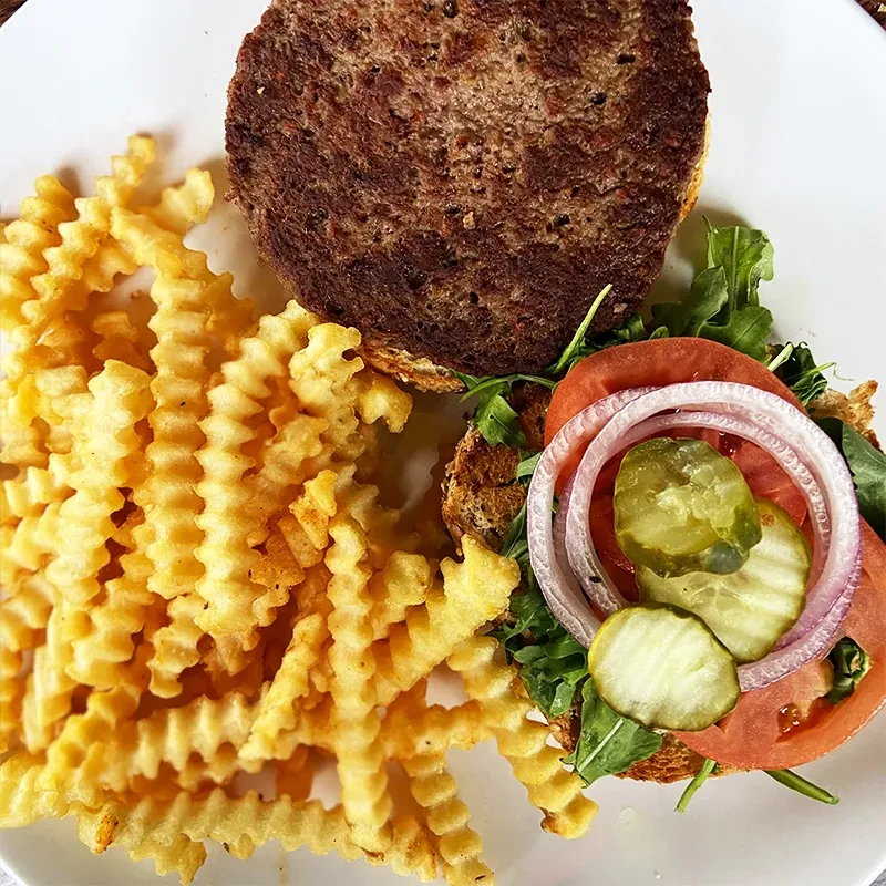 Deconstructed burger with fresh vegetables, patty, and crispy crinkle-cut fries.
