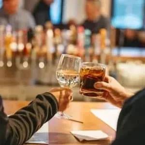 Close-up: two hands toasting a wine glass and a rocks glass.