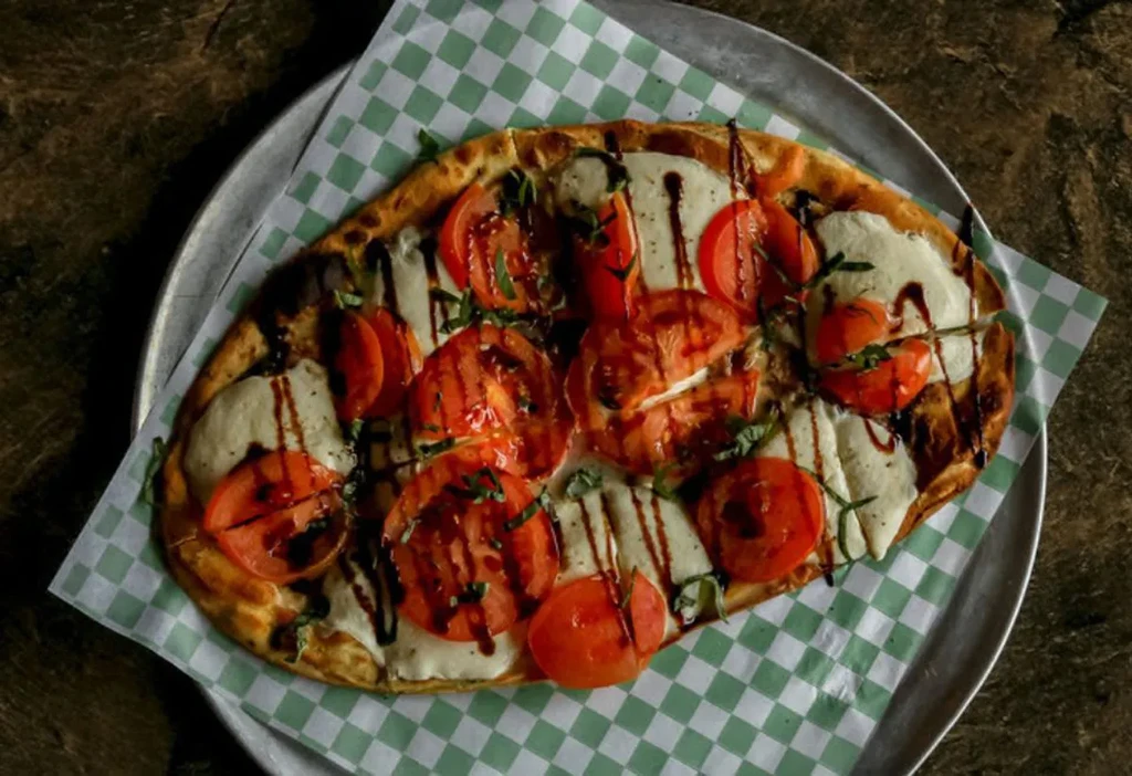 Flatbread pizza topped with tomato, mozzarella, basil, balsamic glaze.