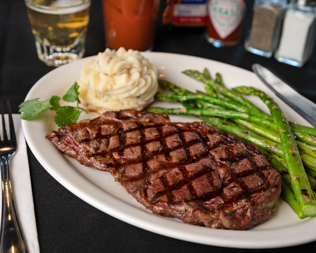 Plated grilled steak, mashed potatoes, and asparagus with condiments.