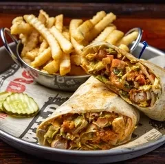 Halved wrap, crinkle-cut fries, and dill pickles served on a metal tray.