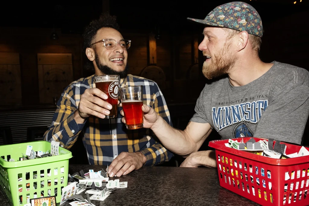 Two bearded men toast beer at a brewery with game pieces.