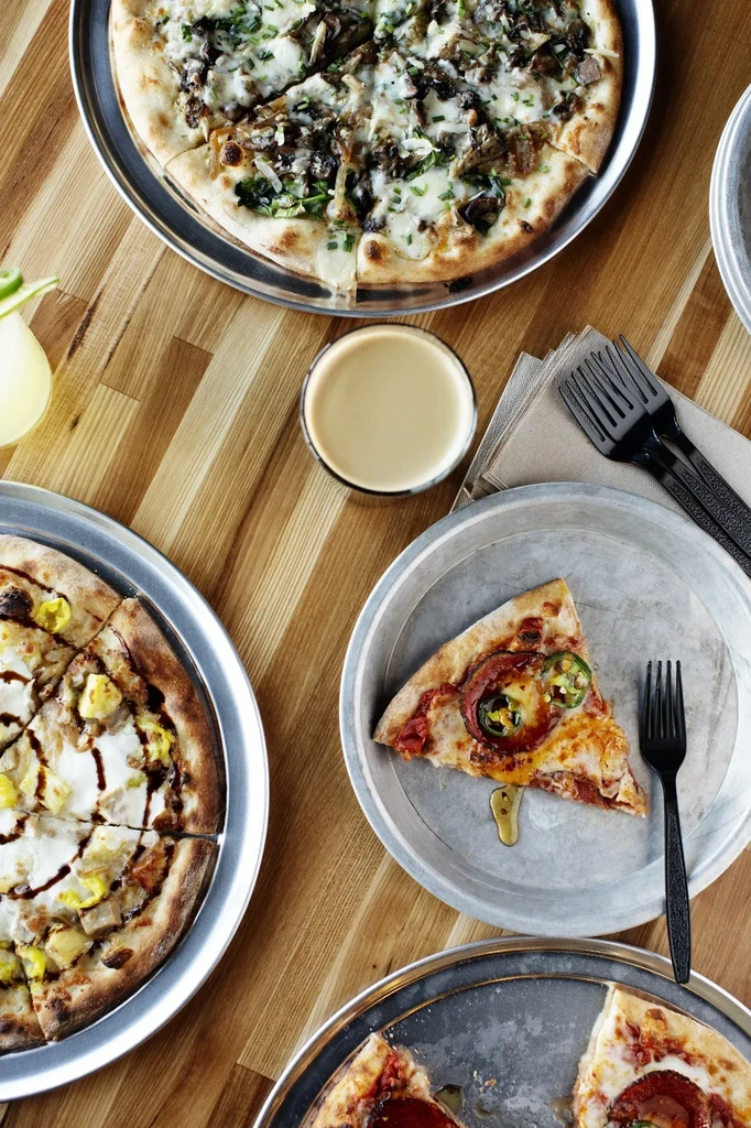 Overhead shot of a wooden table with pizzas and a drink.