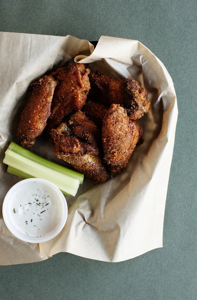 Crispy fried chicken wings, celery, and creamy dip in a container.