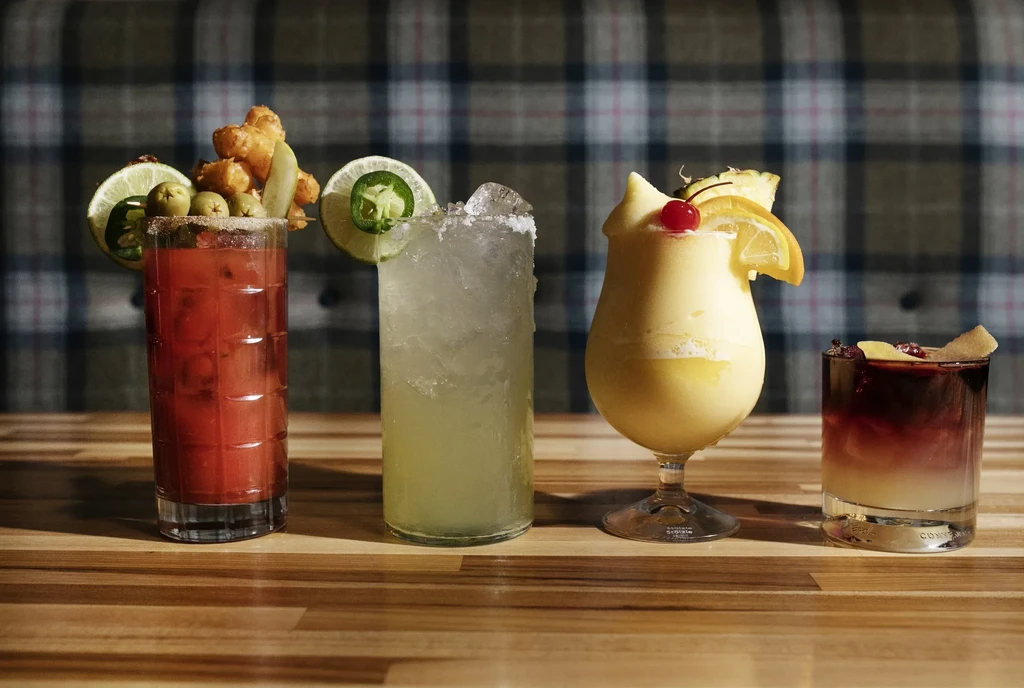 Four distinct, garnished cocktails on a wood table.