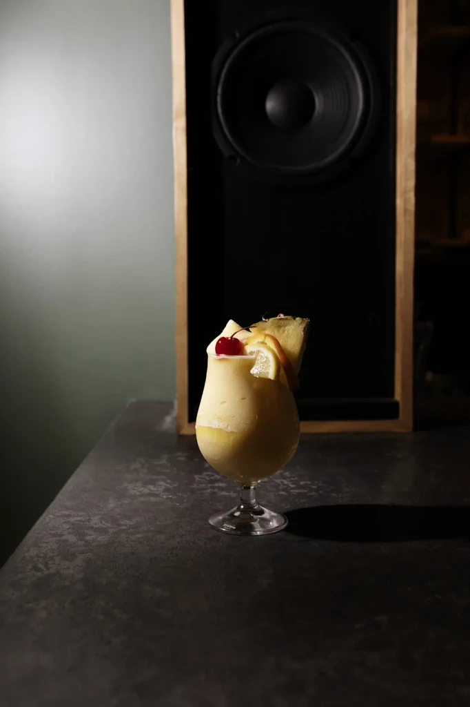 Creamy yellow blended cocktail with cherry, lemon, and pineapple.