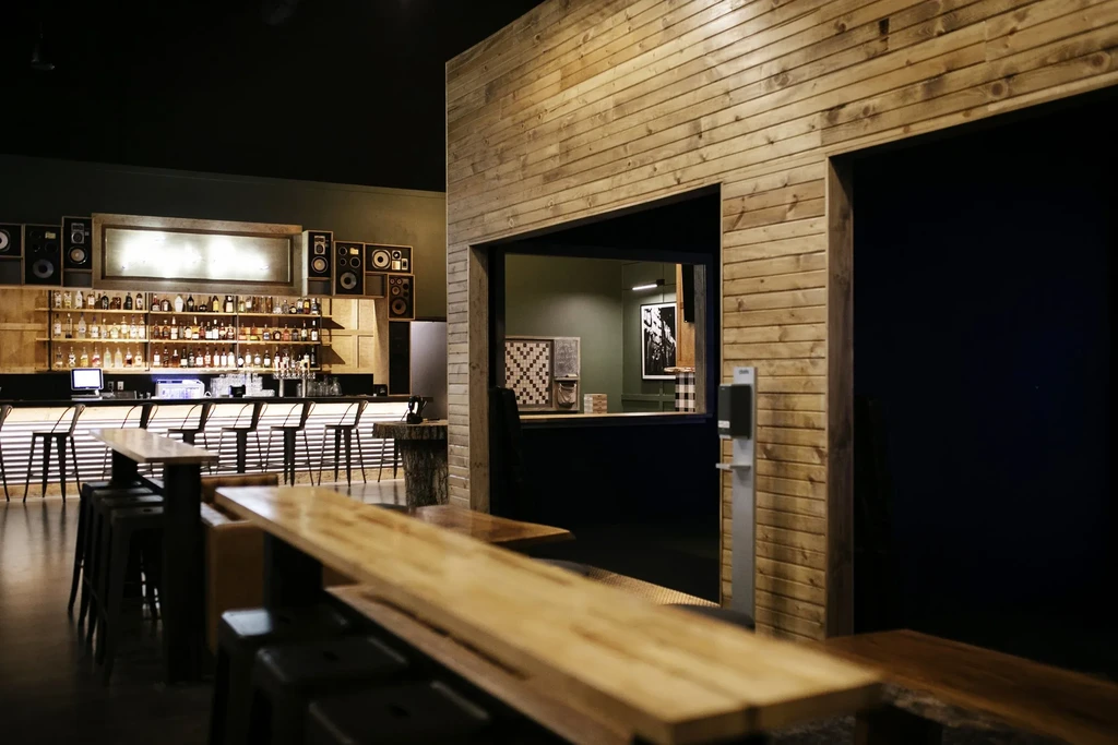 Rustic-modern bar interior with illuminated bottles and vintage speakers.