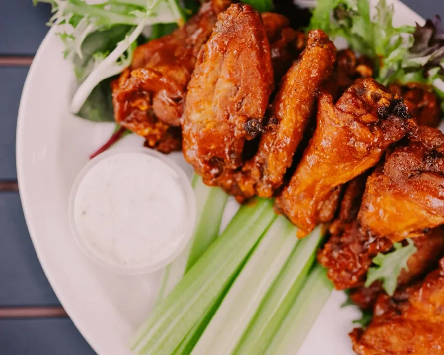 Plate of saucy chicken wings, celery, and creamy dipping sauce.