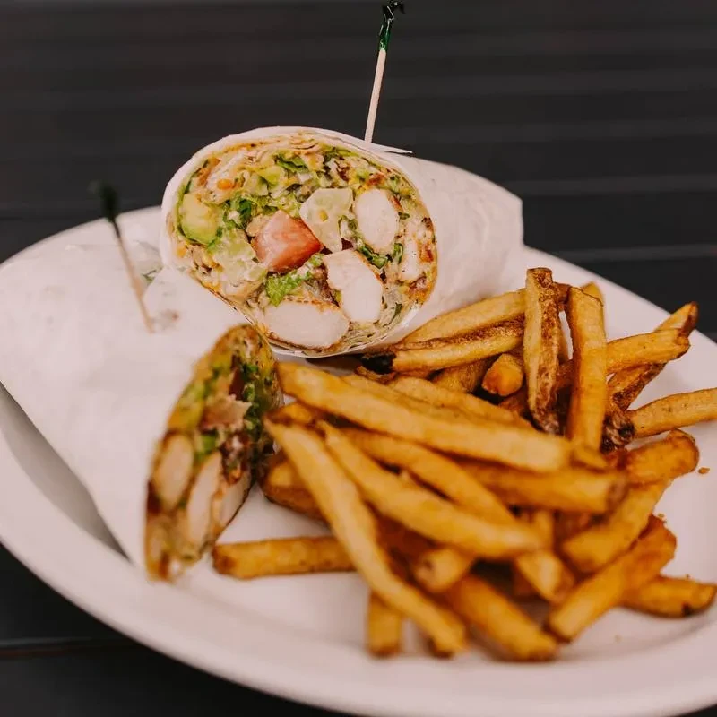 Half-cut chicken avocado wrap and french fries on a white plate.