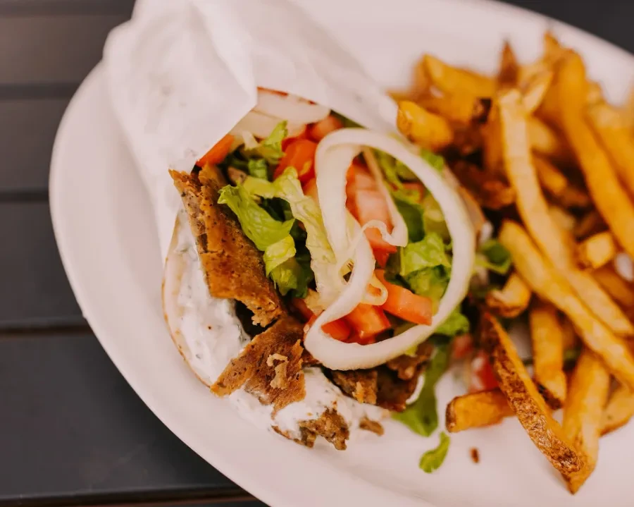 Partially unwrapped gyros kebab with meat, vegetables, sauce, and french fries.