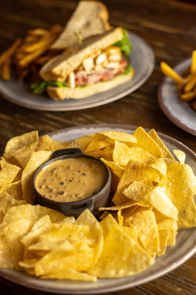 Close-up of tortilla chips and queso, with a sandwich and fries.