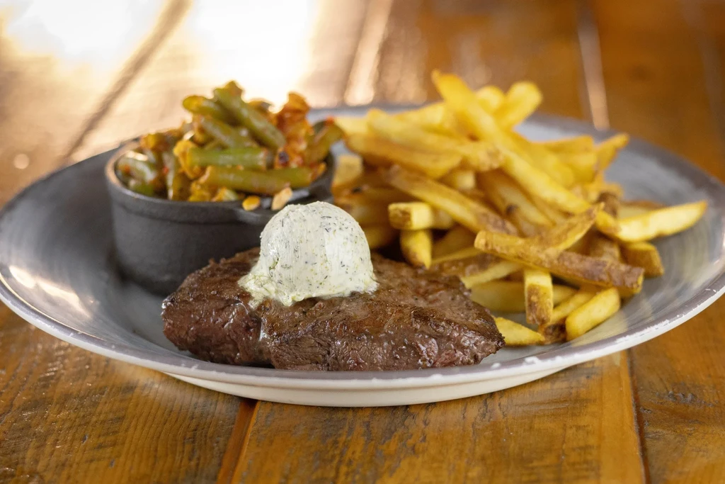 Medium-cooked steak with herb butter, green beans, and french fries.
