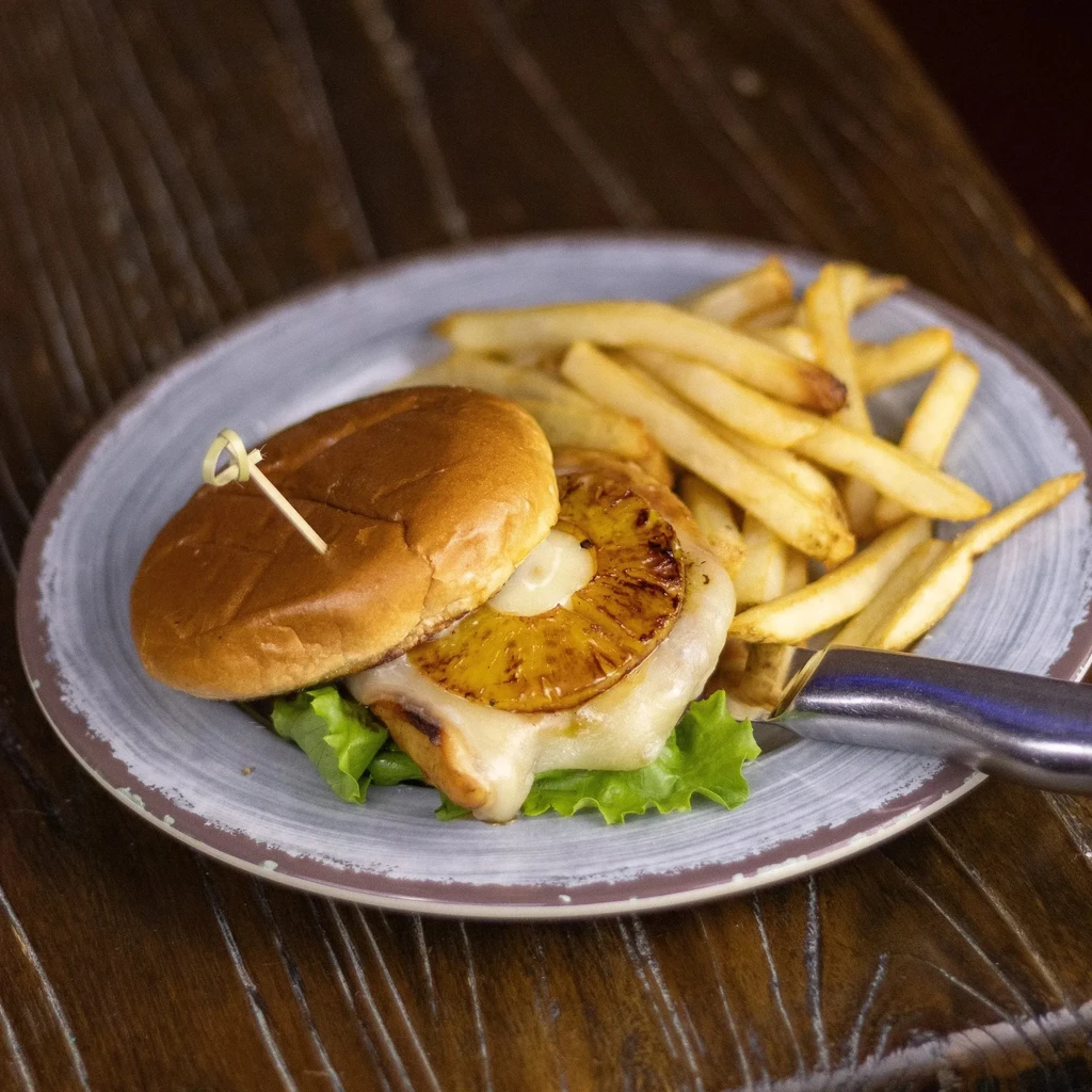 Burger or chicken sandwich with grilled pineapple, melted cheese, and fries.