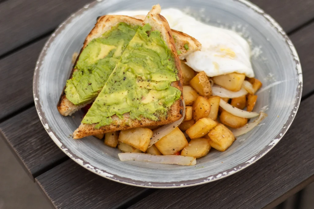 Plate of avocado toast, home fries, and fried eggs on wood.