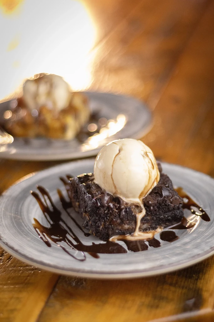 Brownies with vanilla ice cream and chocolate sauce on two plates.