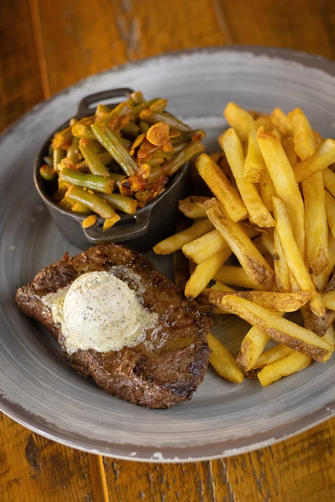 Grilled steak with melting herb butter, fries, and green beans meal.