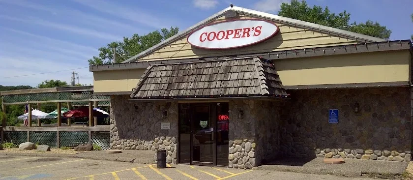 Cooper's restaurant exterior with stone, yellow siding, sign, patio umbrellas.