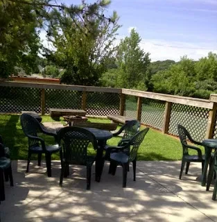 Outdoor patio with tables, chairs, lawn, fire pit, and trees.