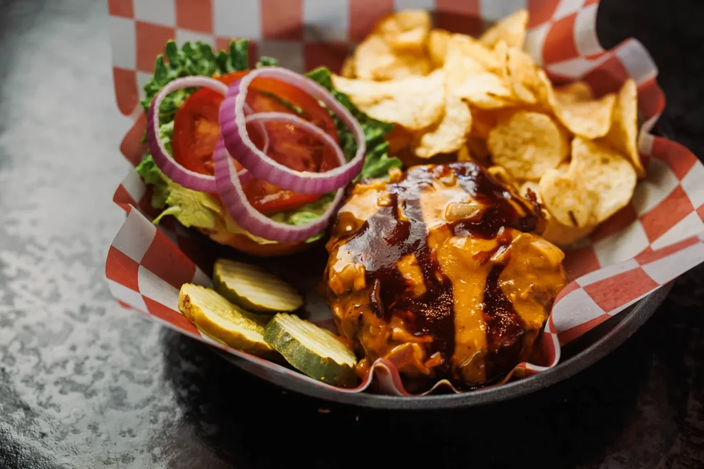 Pulled pork sandwich, potato chips, and pickles in a checkered tray.