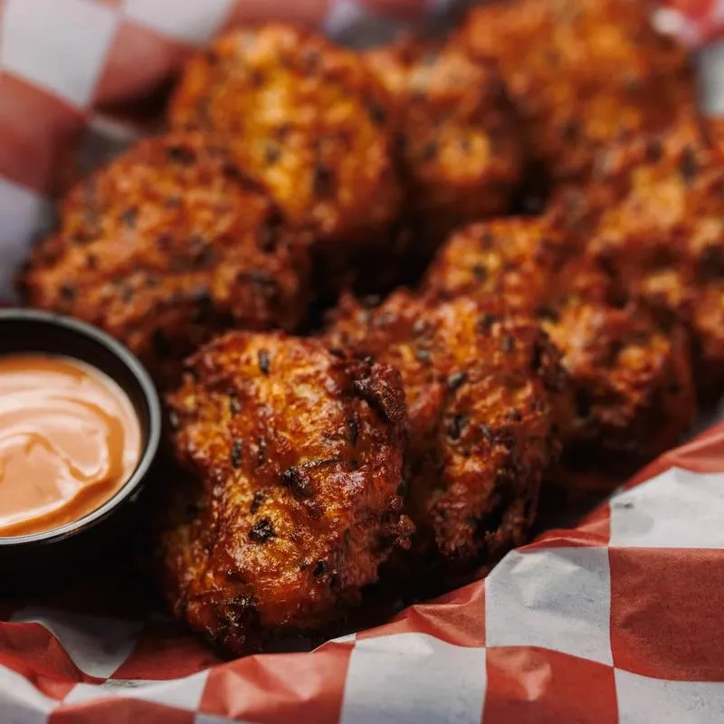 Golden-brown fried fritters with orange dipping sauce on checkered paper.