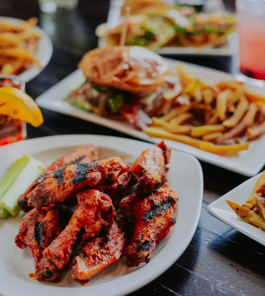 Grilled chicken wings, celery, burger, and fries on a dark table.