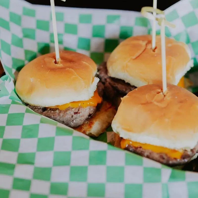 Three mini cheeseburger sliders with melted cheese and skewers.