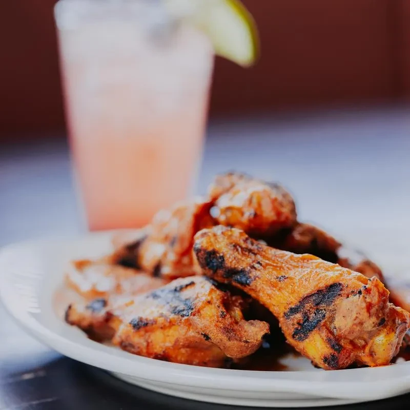 Close-up of char-grilled chicken wings and a frosted pink lime drink.