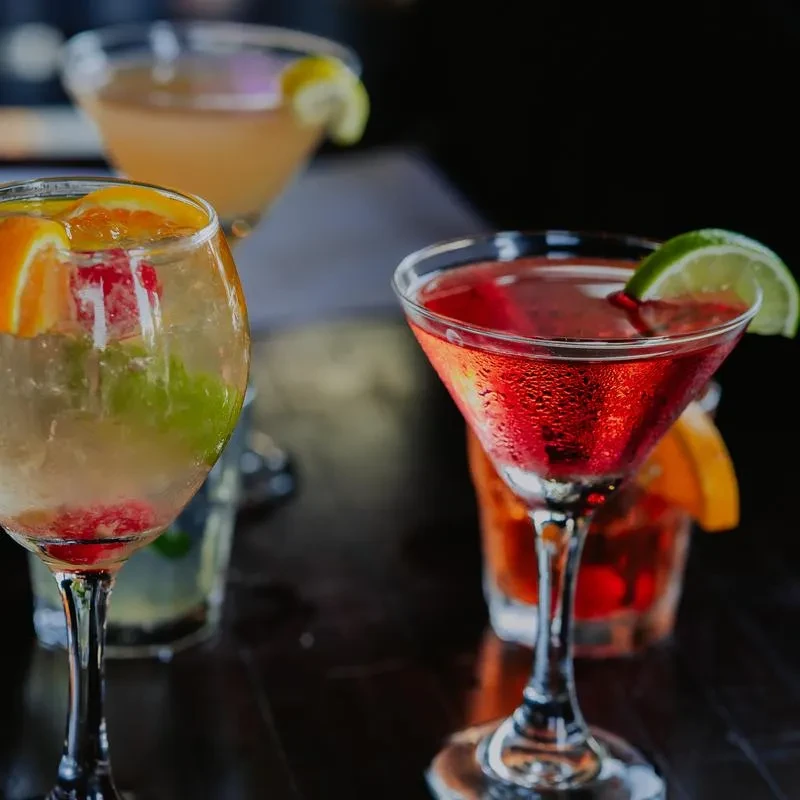 Various vibrant cocktails with fruit garnishes on a reflective bar top.