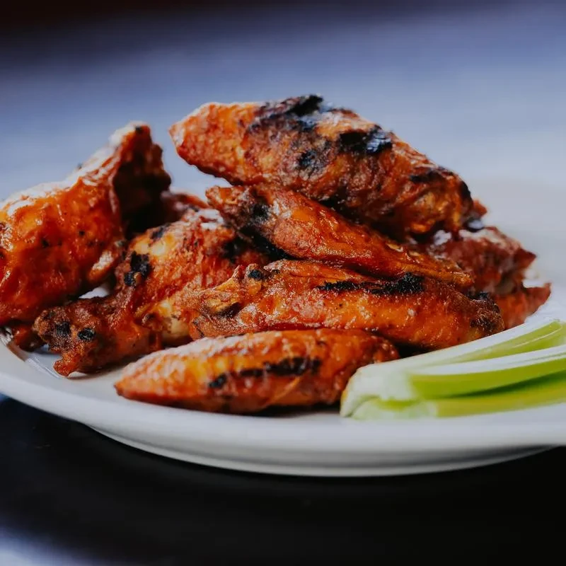 Glossy, grilled chicken wings with celery on a white plate.