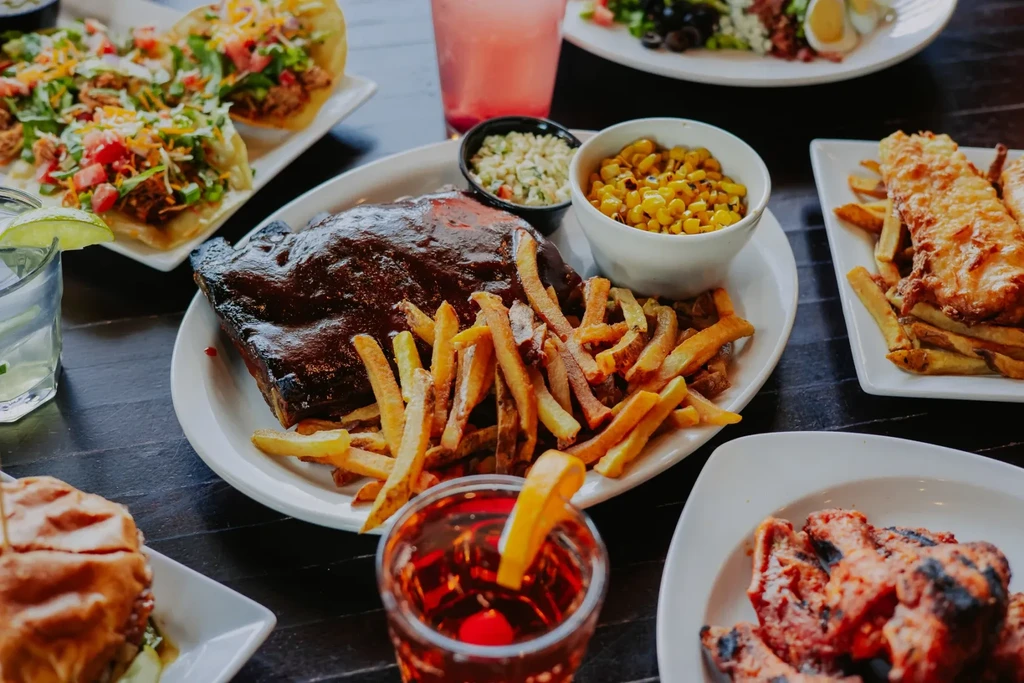 Overhead table shot of barbecue ribs, tacos, and various restaurant dishes.