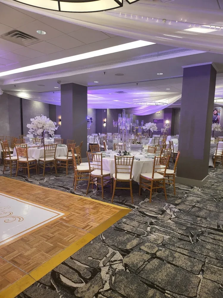 Elegant banquet hall with tables, cherry blossom centerpieces, purple uplighting.