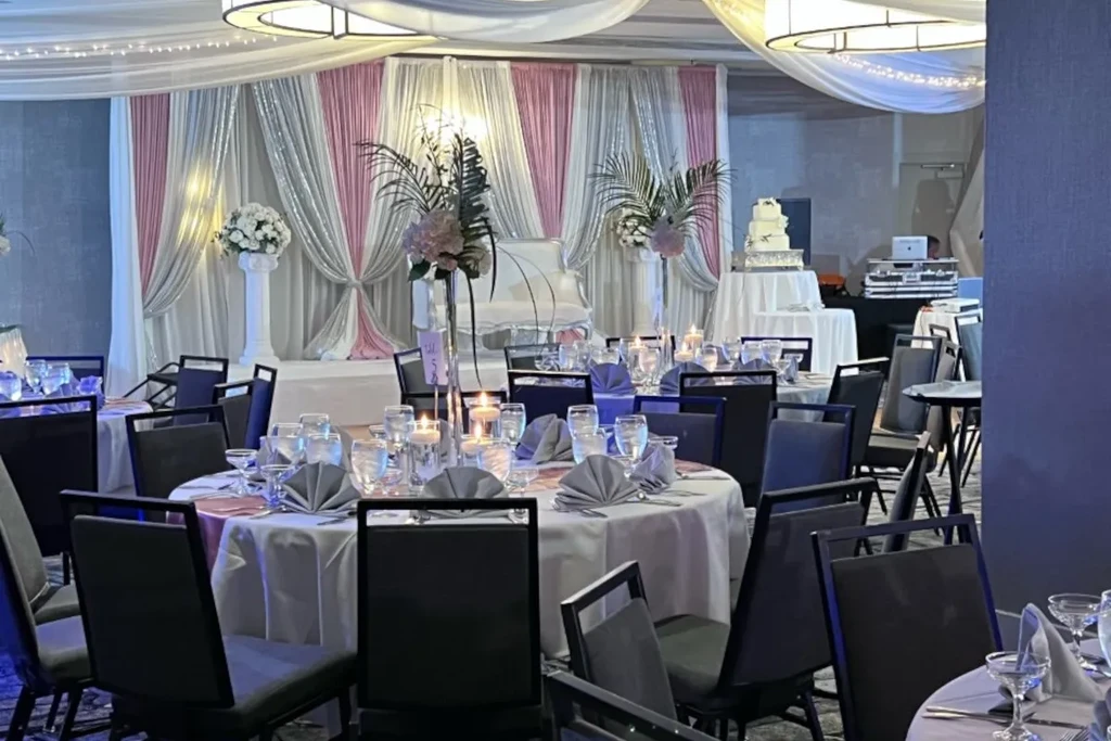 Elegant wedding reception hall with decorated tables, backdrop, cake, and DJ.