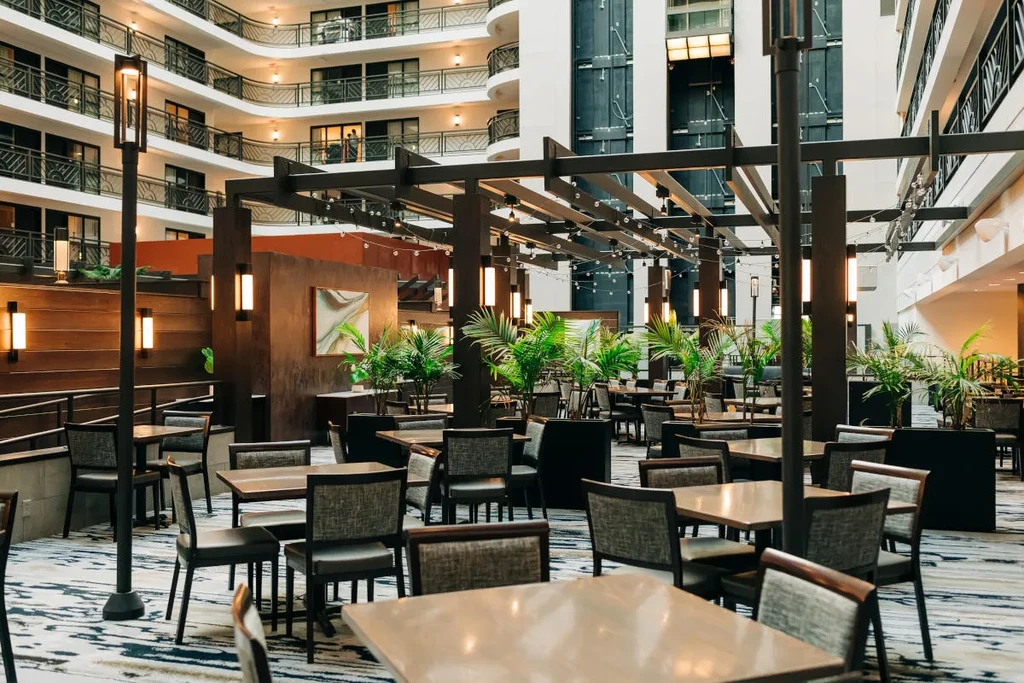 Modern restaurant dining area with tables, lights, and plants inside an atrium.