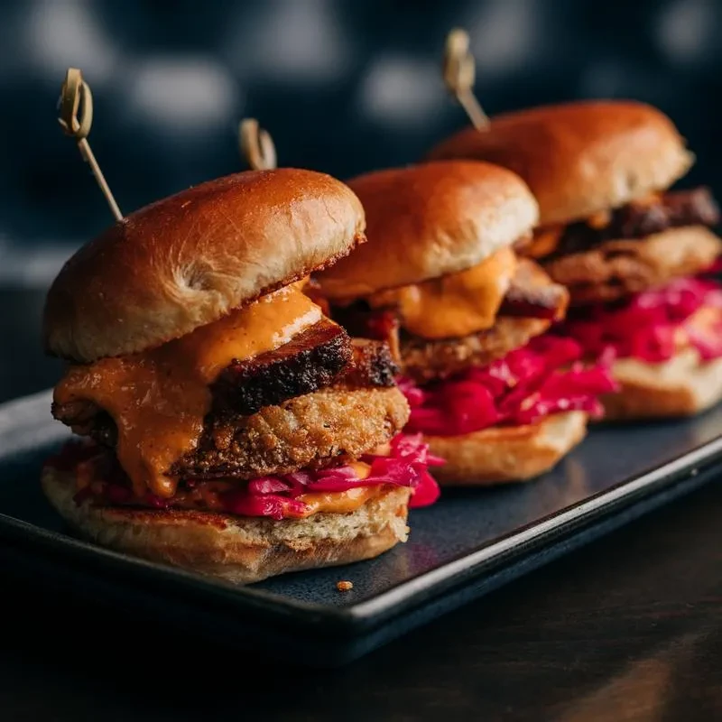 Gourmet sliders with fried patty, braised meat, pink cabbage, orange sauce.
