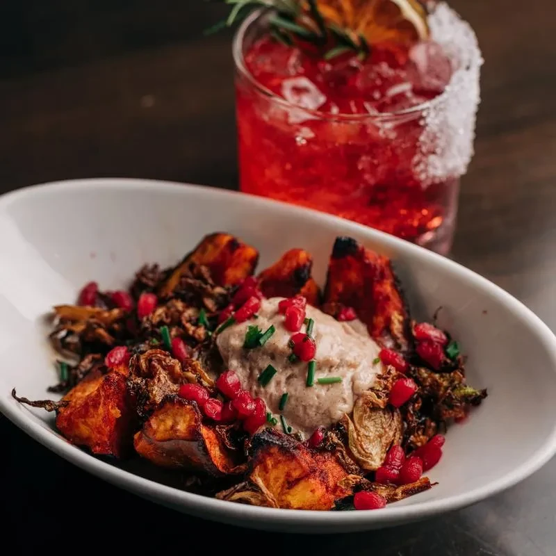 Styled roasted vegetable dish with sauce, pomegranate, and a red cocktail.