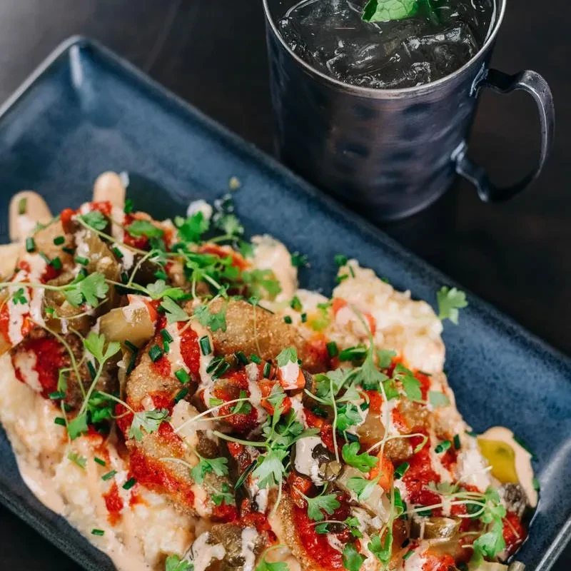 Loaded fries with sauces, herbs, pickled vegetables, and a Moscow Mule.