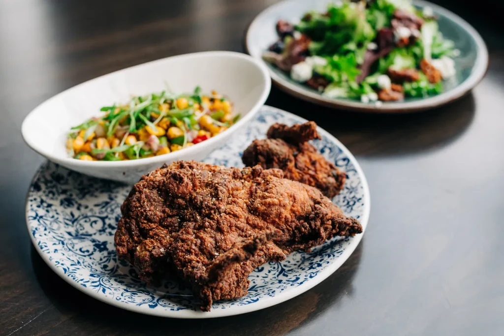 Crispy fried chicken, corn salad, and green salad on a wooden table.