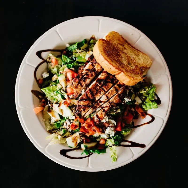 Grilled chicken salad with lettuce, tomatoes, cucumbers, cheese, and toast.
