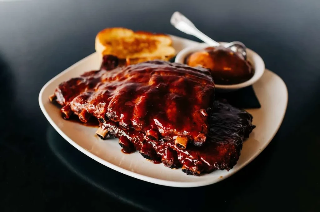 Plate of glistening BBQ ribs with toast and a side dish.
