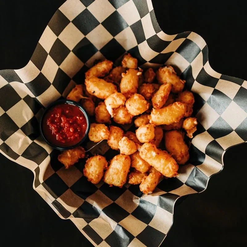 Golden-brown fried food in basket with checkered liner and red dipping sauce.