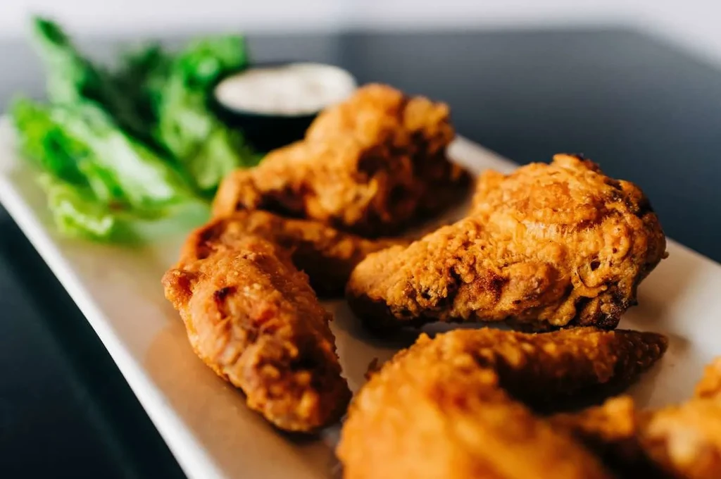 Crispy golden-brown fried chicken wings, lettuce, and sauce on a plate.