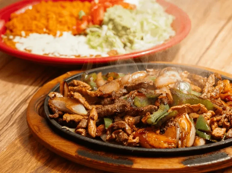 Sizzling fajita platter with meat, peppers, onions, and assorted sides.