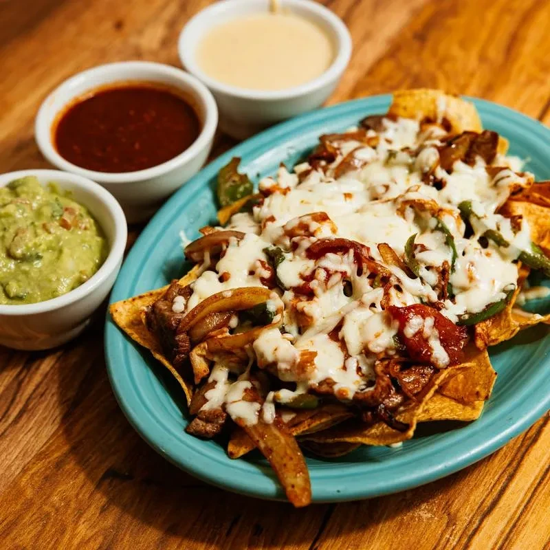 Nachos piled with melted cheese, meat, peppers, and three dipping sauces.