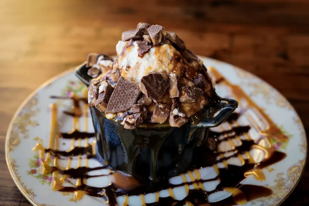Ice cream sundae in handled ceramic pot, chocolate, caramel, and toppings.