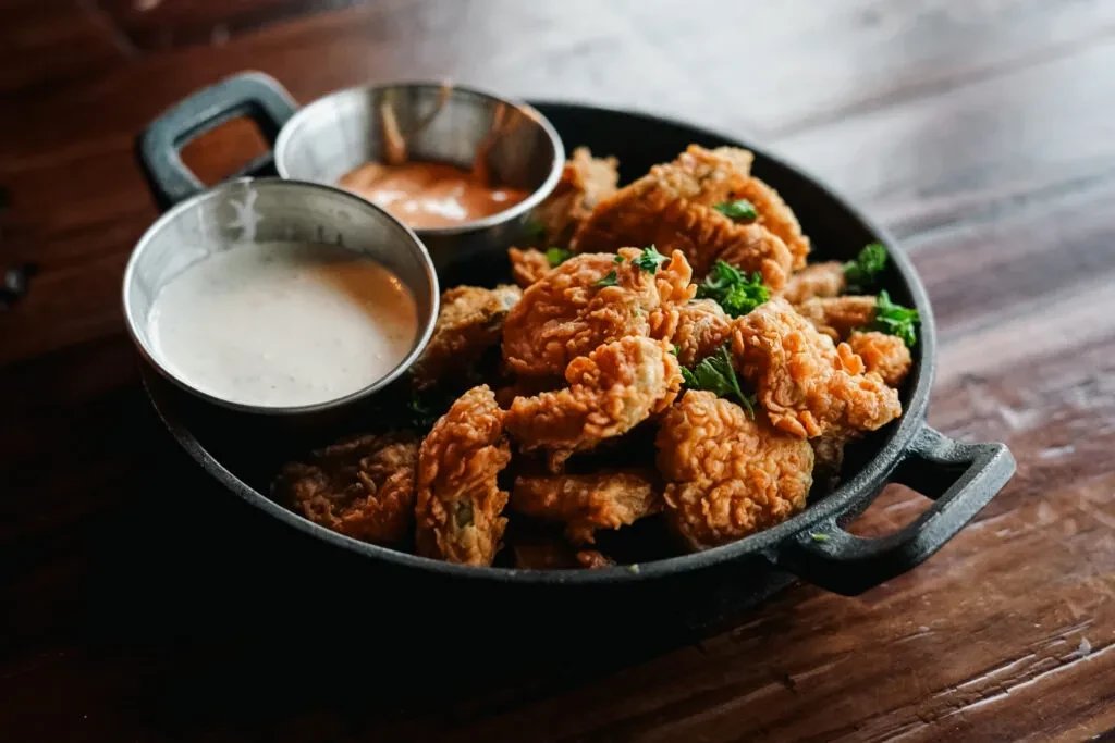 Crispy fried chicken in a skillet with herbs and two sauces.