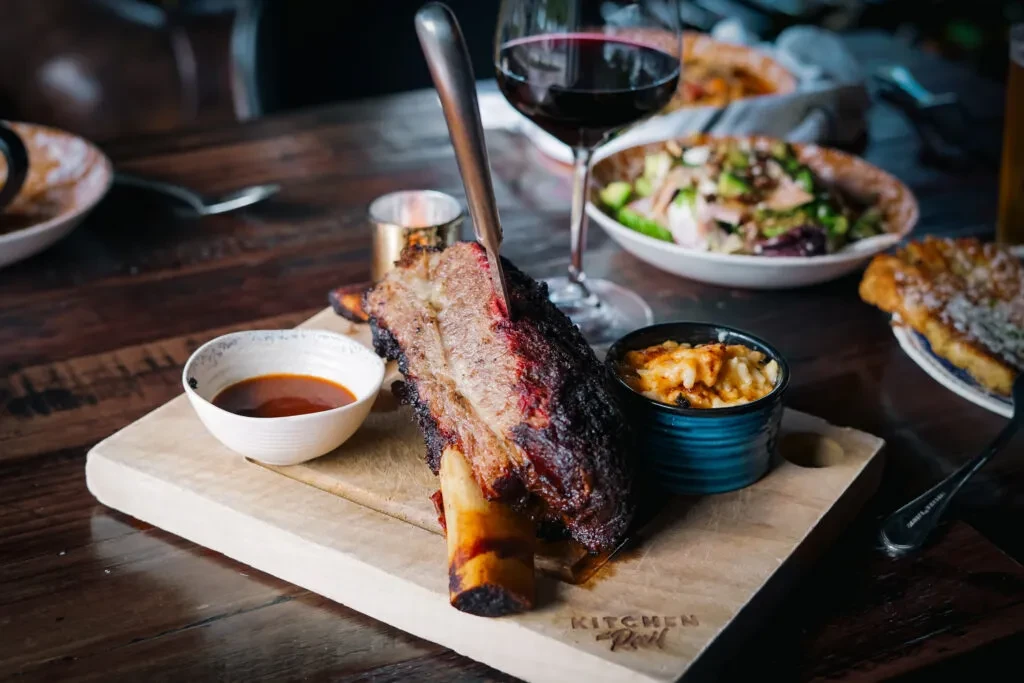 Cooked beef short rib, mac and cheese, sauce, salad, and wine.